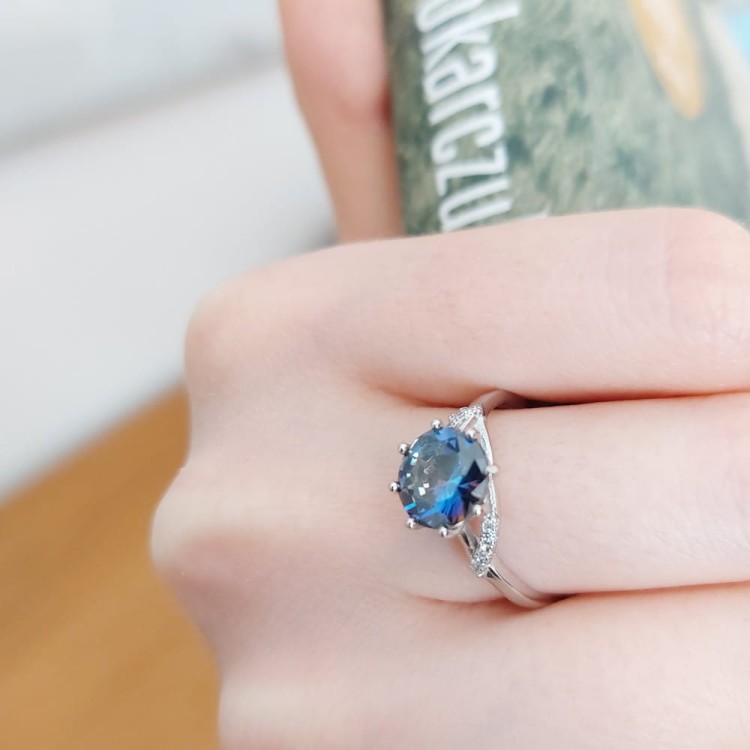 Pierścionek z niebieskim oczkiem, srebrny na kopułce w typie Tiffany. Drobne cyrkonie u dołu . Obrączka srebrna rodowana zwężająca się przy kopułce.